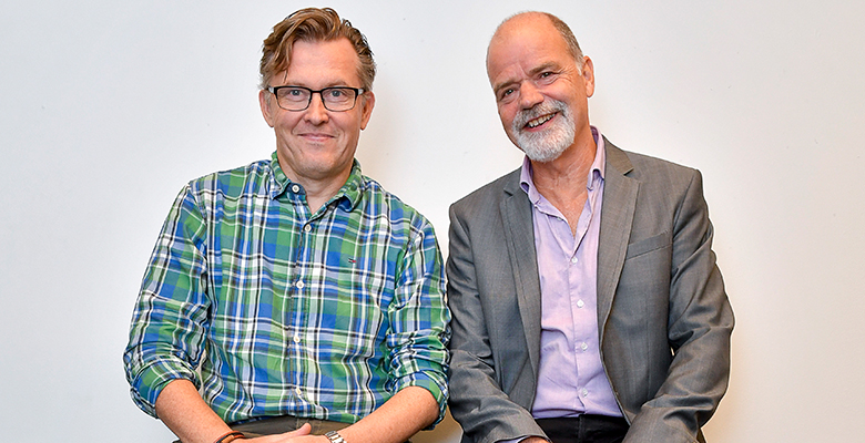 Håkan och Lasse sitter bredvid varandra, tittar och ler in i kameran
